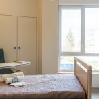 un chambre lumineuse avec un lit, un fauteuil, une grande fenetre et un petit bureau