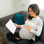 Une femme enceinte assise sur son canapé, regardant le calendrier de grossesse