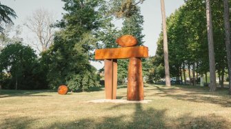 dans un parc, une grande sculpture en bois à la forme d'une porte