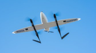 un drone blanc aux helices noires est en vol sur fond de ciel bleu