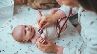 un bébé allongé sur le dos est ausculté par une femme vêtue d'une blouse blanche