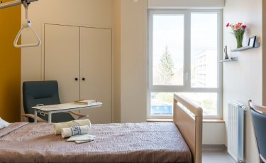 un chambre lumineuse avec un lit, un fauteuil, une grande fenetre et un petit bureau
