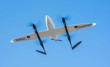 un drone blanc aux helices noires est en vol sur fond de ciel bleu