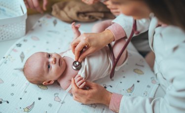un bébé allongé sur le dos est ausculté par une femme vêtue d'une blouse blanche
