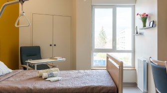 un chambre lumineuse avec un lit, un fauteuil, une grande fenetre et un petit bureau