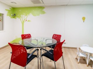 dans une pièce claire une table en verre est installée au centre. Autour des chaises rouges. A gauche de l'image un glace sans tain