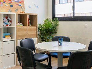 dans une pièce lumineuse, des jeux sont posés sur des étagères. Au centre de l'image une table ronde avec des chaises autour