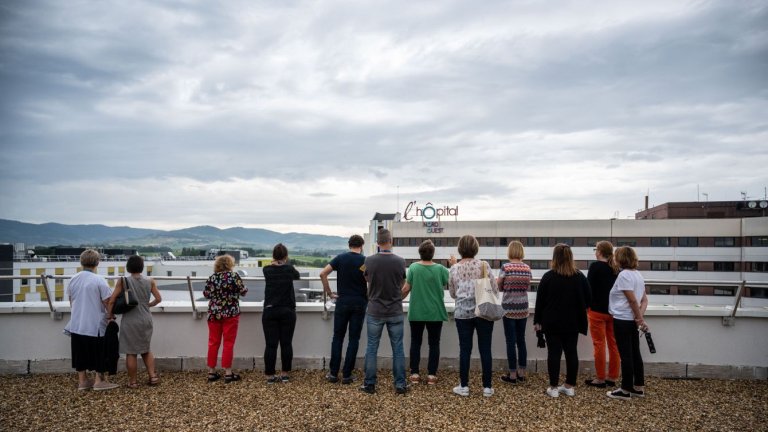 sur un toit, un groupe de personnes de dos regardent l'hôpital de Villefranche