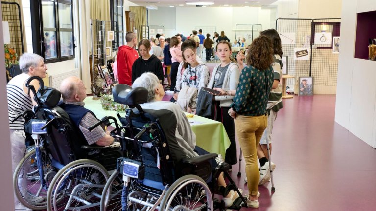 dans une salle d'exposition, des personnes âgées et des collégiens discutent