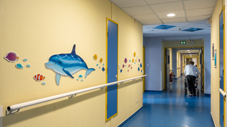 un grand dauphin précédé et suivi par de petits poissons colorés sont dessinés sur un mur jaune de couloir