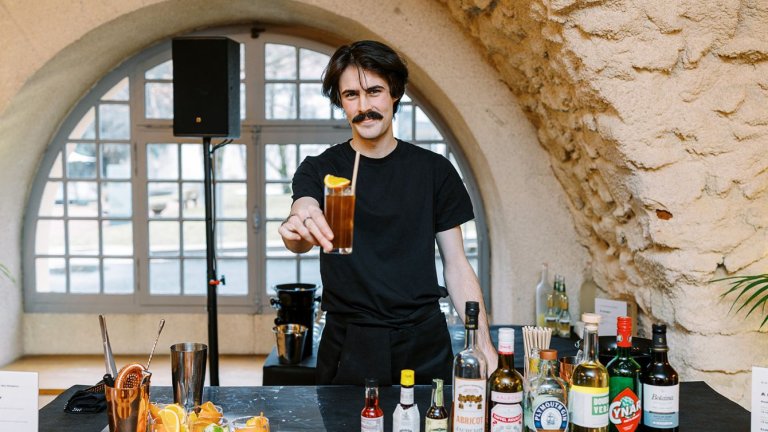 un jeune homme tend un verre à cocktail avec une paille. 