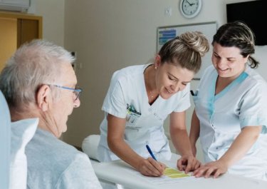 deux infirmières discutent avec un patient installé sur son lit
